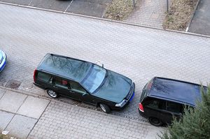 Eine Reihe von Autos,von denen zwei eine Fußgängerfurt mit abgesenkten Bordstein zuparken. An der Furt ist der Abstand zwischen den Fahrzeugen am geringsten.